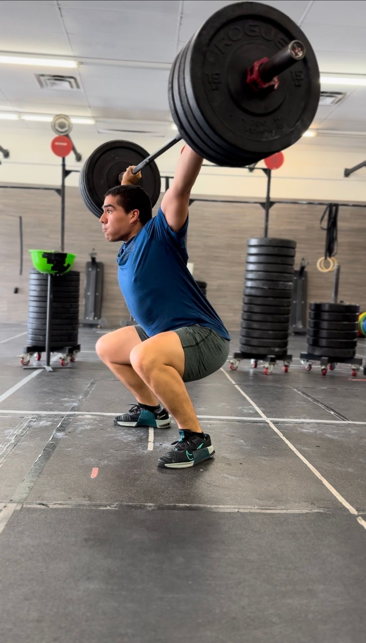 A man is squatting with a barbell over his head in a gym.